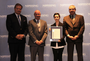 Dave Marshall Leadership Awards ceremony photo of an award recipient holding a framed certificate in front of a Nipissing University backdrop