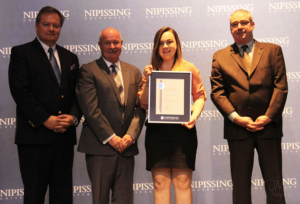 Dave Marshall Leadership Awards ceremony photo of an award recipient holding a framed certificate in front of a Nipissing University backdrop