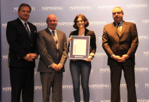 Dave Marshall Leadership Awards ceremony photo of an award recipient holding a framed certificate in front of a Nipissing University backdrop