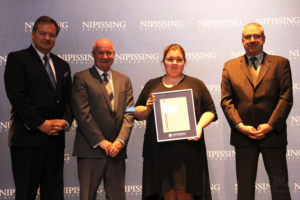 Dave Marshall Leadership Awards ceremony photo of an award recipient holding a framed certificate in front of a Nipissing University backdrop