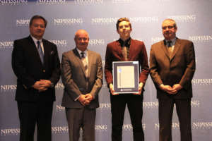 Dave Marshall Leadership Awards ceremony photo of an award recipient holding a framed certificate in front of a Nipissing University backdrop