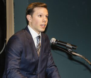 A man in a suit and tie speaking into a microphone at a podium